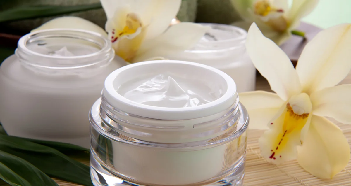 Open jar of luxurious white skincare cream surrounded by elegant orchid flowers, creating a spa-like ambiance.